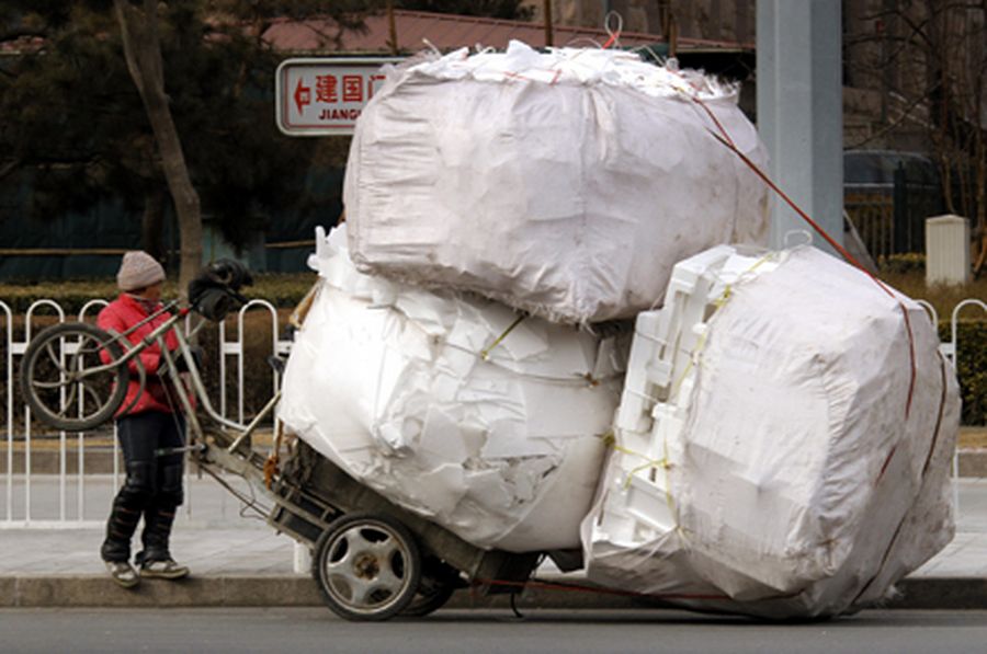 A recyclable materials collector stands in front of her overloaded tricycle on a main street in cent